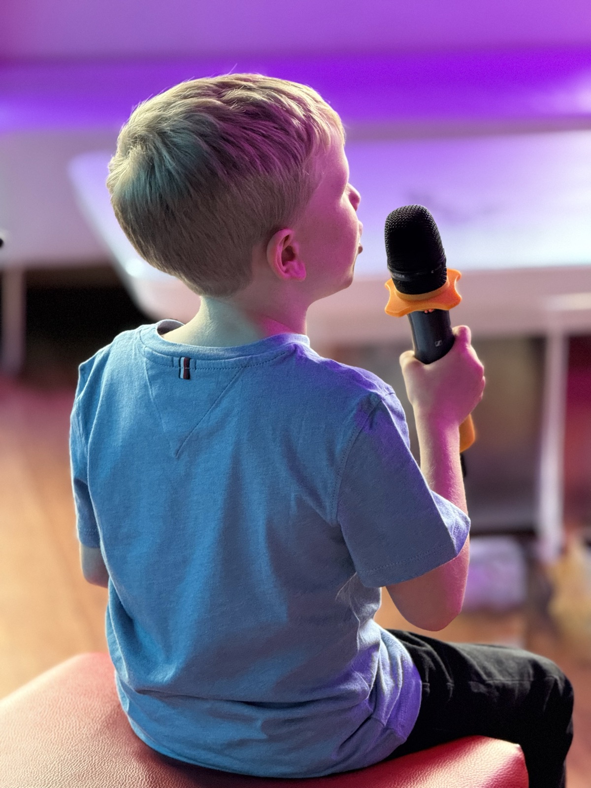 Un jeune chanteur tient son micro sous les lumières violettes de la salle.