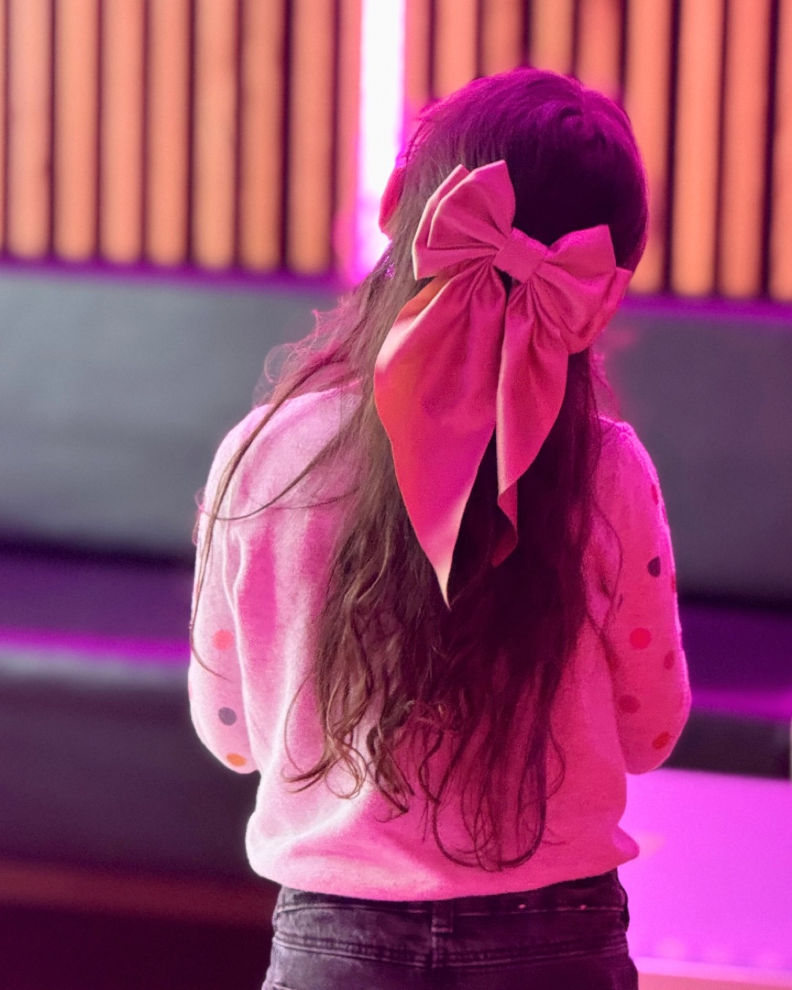 Une petite chanteuse au grand nœud rose dans la salle de karaoké.